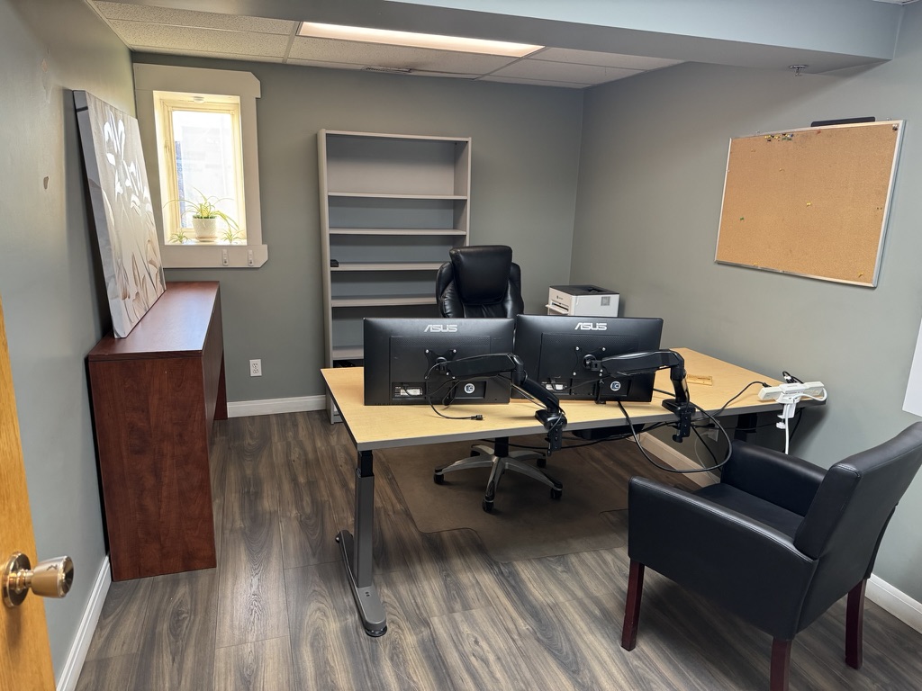 Private office at 250 Charlesworth Ave Cochrane with sit-stand desk, dual monitors, bookshelf and leather chair