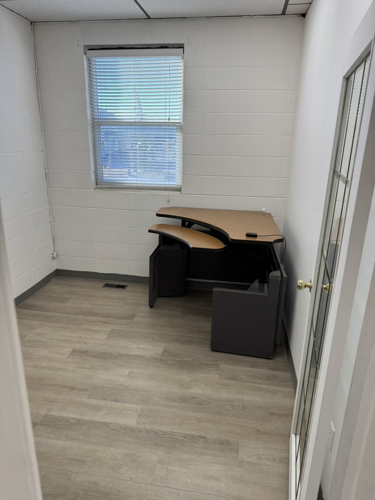 Single L-shaped desk in a private office at River Ave, with window and frosted glass door