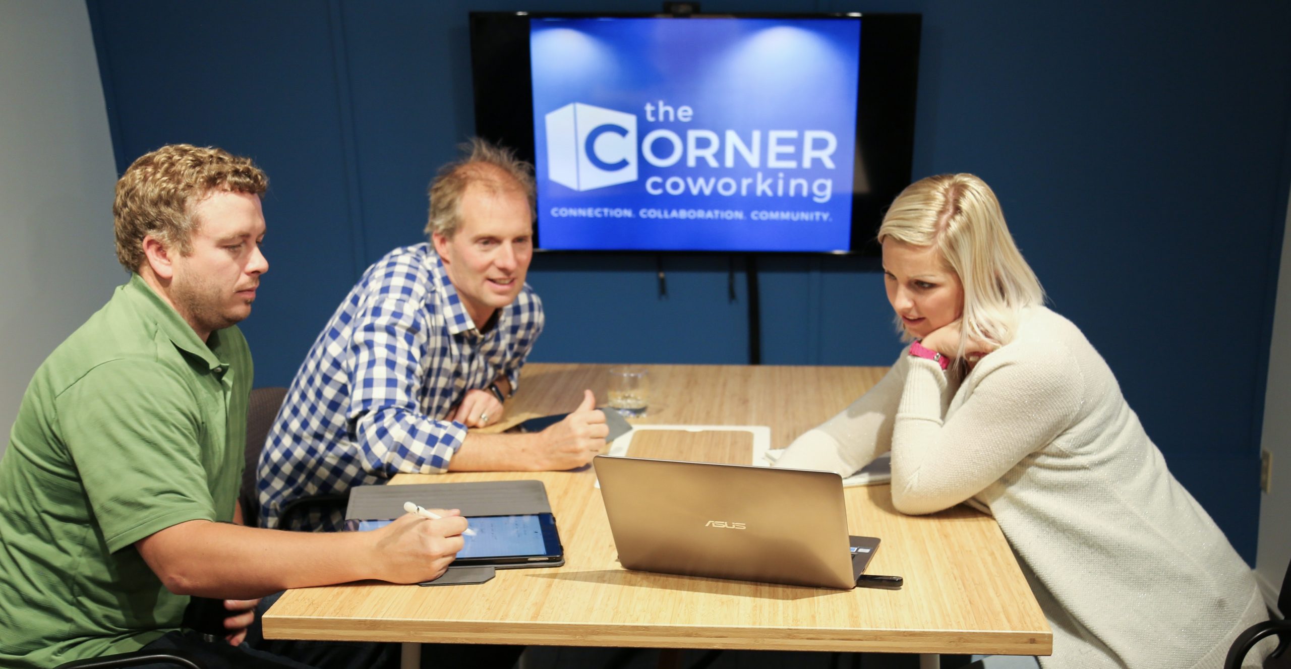 Members collaborating around a shared table with laptops at The Corner Coworking in Cochrane, Alberta